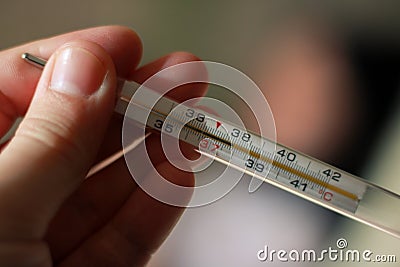 An alcohol thermometer shows a temperature of 37.9 on a blurred background of a sick girl lying on a bed. Check the temperature. Stock Photo