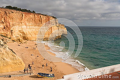 Golden cliffs tower over a sandy beach with scattered visitors in Algarve, Portugal Editorial Stock Photo