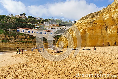 Visitors enjoy a day at the beach beneath the cliffside homes of Algarve Editorial Stock Photo