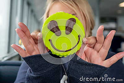 Blonde adult woman holds up an alien themed sugar cookie to cover her face. Concept for funny, hiding, acting goofy Stock Photo