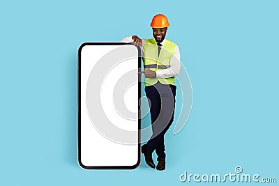 All For Construction. Happy Black Engineer Pointing At Big Blank Smartphone Screen Stock Photo