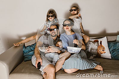 All family father with baby on his arms, mother and two daughters in the special glasses watching tv and eating popcorn Stock Photo