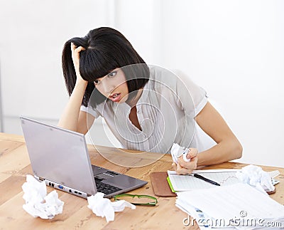All her work has amounted to nothing. A shocked businesswoman looking at her laptop screen amidst crumpled documents. Stock Photo