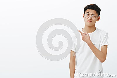 Is it all you got. Portrait of unimpressed doubtful young smart asian guy in glasses and white t-shirt pointing left Stock Photo