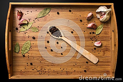 Allspice in a wooden spoon on a wooden tray. Garlic and bay leaf. View from above. Seasoning flavoring for meat and food. Stock Photo