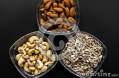 Almond, cashew and sunflower seeds in a small plates which standing on a black table. Nuts is a healthy vegetarian Stock Photo