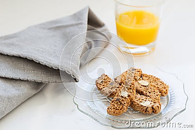Almond and chocolate biscotti in vintage scalloped glass plate, with grey serviette and small glass of orange juice Stock Photo