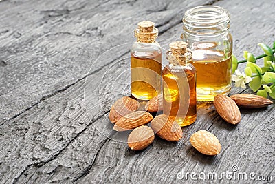 Almonds oil in various glass containers and pile of roasted almonds on black wooden plank. Stock Photo