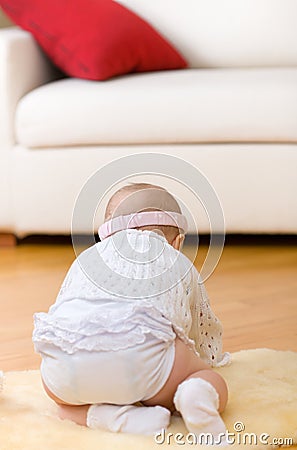 Alone baby girl sit down on fur at hardwood floor Stock Photo