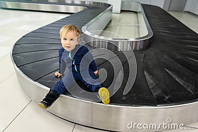 Alone cute caucasian blond toddler boy sitting on empty airport arrival terminal luggage conveyor belt. Lost found child. Travel Stock Photo