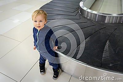 Alone cute caucasian blond toddler boy standing near empty airport arrival terminal luggage conveyor belt. Lost found child. Stock Photo