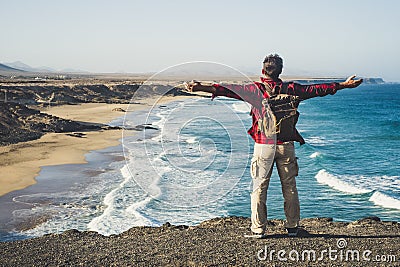 Alone happy traveler with backpack people man enjoying the destination place beach standing on a cliff and opening arms for Stock Photo