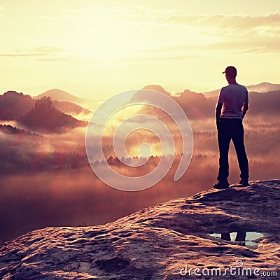 Alone hiker in white shirt and red cap stand on peak of rock in rock empires park and watch over misty and foggy valley to Sun. Th Stock Photo