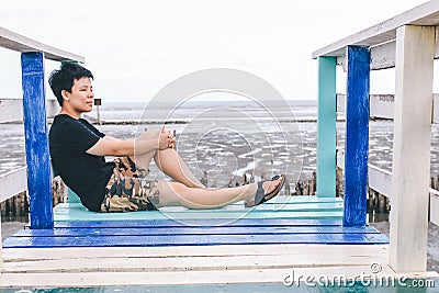 Alone traveler relax siting on colorful rainbow wooden bridge extends into the mangrove sea tourist attractions in Thailand, Stock Photo