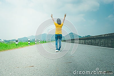 Alone woman traveler or backpacker walking along countryside road along side with reservoir, she raise hands over head. Stock Photo