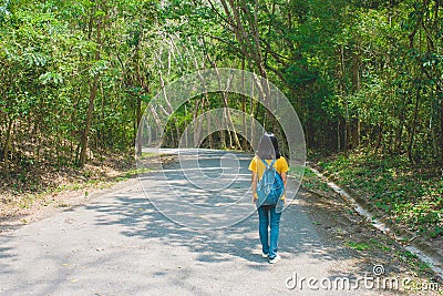 Alone woman traveller or backpacker walking along contryside road among green trees. Stock Photo