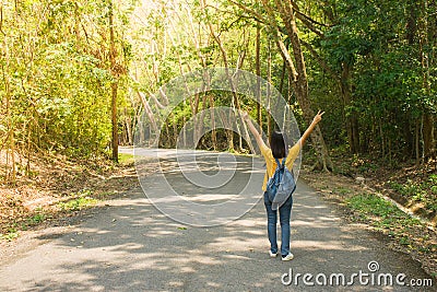 Alone woman traveller or backpacker walking along contryside road among green trees, she has feeling happiness. Stock Photo