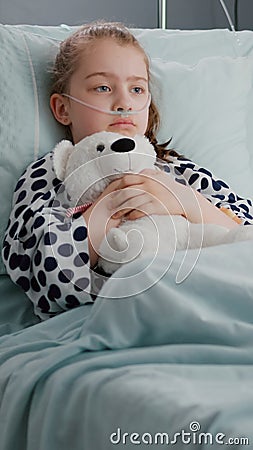 Alone worried child patient wearing oxygen nasal tube resting in bed holding teedy bear Stock Photo