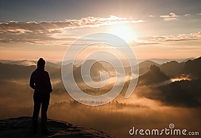 Alone young girl tourist feast autumn daybreak on the sharp corner of sandstone rock and watch over misty valley to Sun. Stock Photo