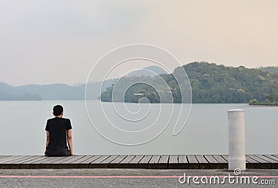 Alone young man sitting on wooden walkway looking to the mountain in the lake with sunset background Editorial Stock Photo