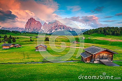 Alpine green fields and wooden chalets at sunset, Dolomites, Italy Stock Photo