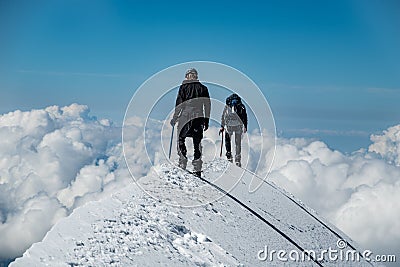 Alpinists on Aiguille de Bionnassay summit - extremely narrow snow ridge above clouds, Mont Blanc massif, France Stock Photo