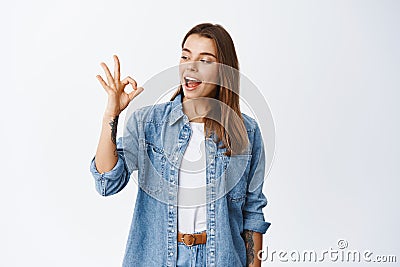 Alright. Smiling cute girl showing okay sign and say yes, approve something good, like and agree, standing pleased Stock Photo