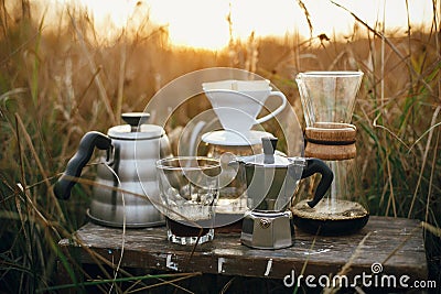 Alternative coffee brewing outdoors in travel. Steel kettle, hot coffee in cup, coffee dripper, geyser maker, glass flask with Stock Photo