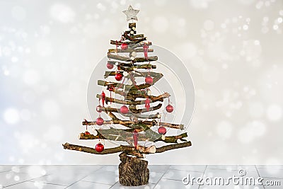Alternative homemade Christmas tree made of rustic raw wood branches, decorated with fairy lights and red baubles, sustainable Stock Photo
