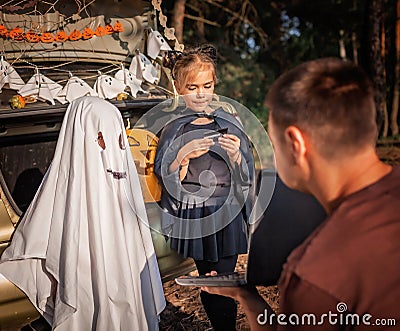 Online Halloween celebration. Kids getting mobile money on card at party in trunk of car Stock Photo