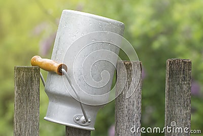 An aluminum pot hangs on an old fence. Dishes for milk and other drinks. Life in the village Stock Photo