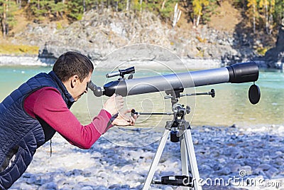 Tourist looks into distance through telescope at mountain river background in mountains Stock Photo