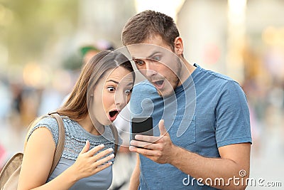 Amazed couple watching on line media in a phone Stock Photo