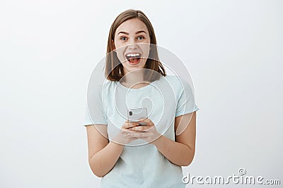 Amazed and excited attractive young european female model smiling broadly from great news received via internet holding Stock Photo