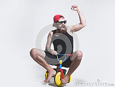 Amazed funny bicycle rider, excited man on colorful bicycle toy in sunglasses, cap. Guy riding childs tricycle. Stock Photo