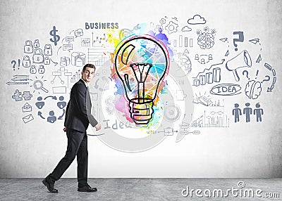 Amazed handsome businessman walking along the concrete wall with colorful business idea light bulb sketch and business flowchart. Stock Photo