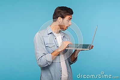 Amazed shocked man in worker denim shirt doing freelance job on laptop, typing email or surfing internet Stock Photo