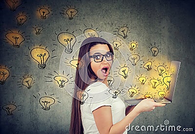 Amazed woman holding a laptop with brilliant ideas light bulbs flying out Stock Photo