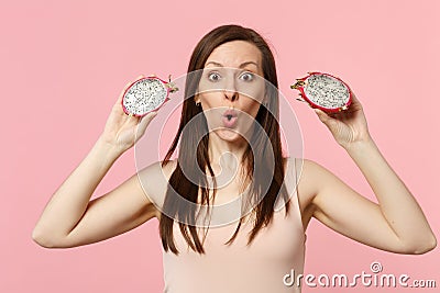 Amazed young woman holding in hands two halfs of fresh ripe pitahaya, dragon fruit isolated on pink pastel wall Stock Photo