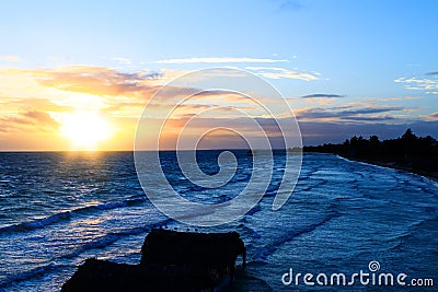 Amazing beach at sunrise or sunset. Background of a seashore with palm trees and blue water in the early morning. Multicolored Stock Photo