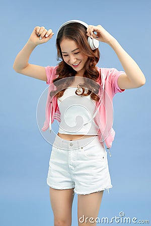 Amazing charming summer young woman in jeans shorts over colorful blue background. Dancing, listening to music with headphones Stock Photo