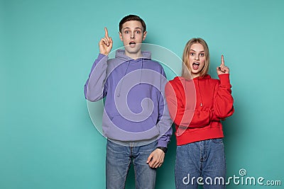 Amazing emotional young couple friends in casual clothes posing with open mouth pointing up with fingers Stock Photo