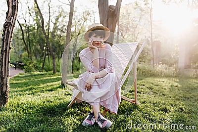 Amazing girl with short dark hair sitting on garden chair with legs crossed on wonderful nature background. Portrait of Stock Photo