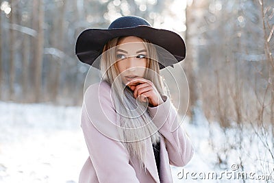 Amazing glamorous pretty beautiful young woman in a luxurious black hat in a stylish pink warm coat posing on a sunny day Stock Photo