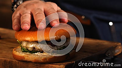 Amazing homemade hamburger with greens, tomatoes, juicy chicken meat and berries on the wooden board with chef in blue Stock Photo