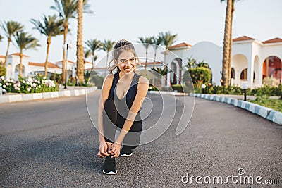 Amazing joyful young woman in sportwear preparing to running on street in sunny morning. Smiling to camera, active Stock Photo