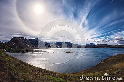 Amazing panoramic landscape, Highlands of Iceland with lake in volcanic mountains, blue cloudy sky and solar halo, Iceland Stock Photo