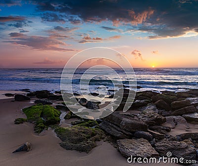 Amazing sunset on the ocean. View of dramatic cloudy sky and stony coast. Portugal. Stock Photo
