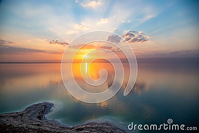 Sunset over Dead sea, view from Jordan to Israel and Mountains of Judea. Reflection of sun, skies and clouds. Salty beach, salt. Stock Photo