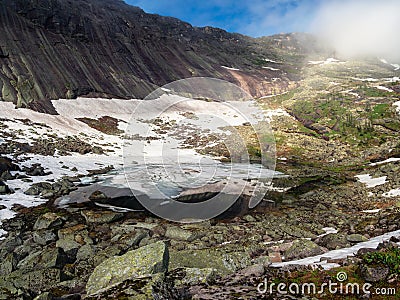 Amazing view of misty Black Lake with huge stones on the shore in Ergaki Nature Park. Summer landscape of crystal blue lake with Stock Photo